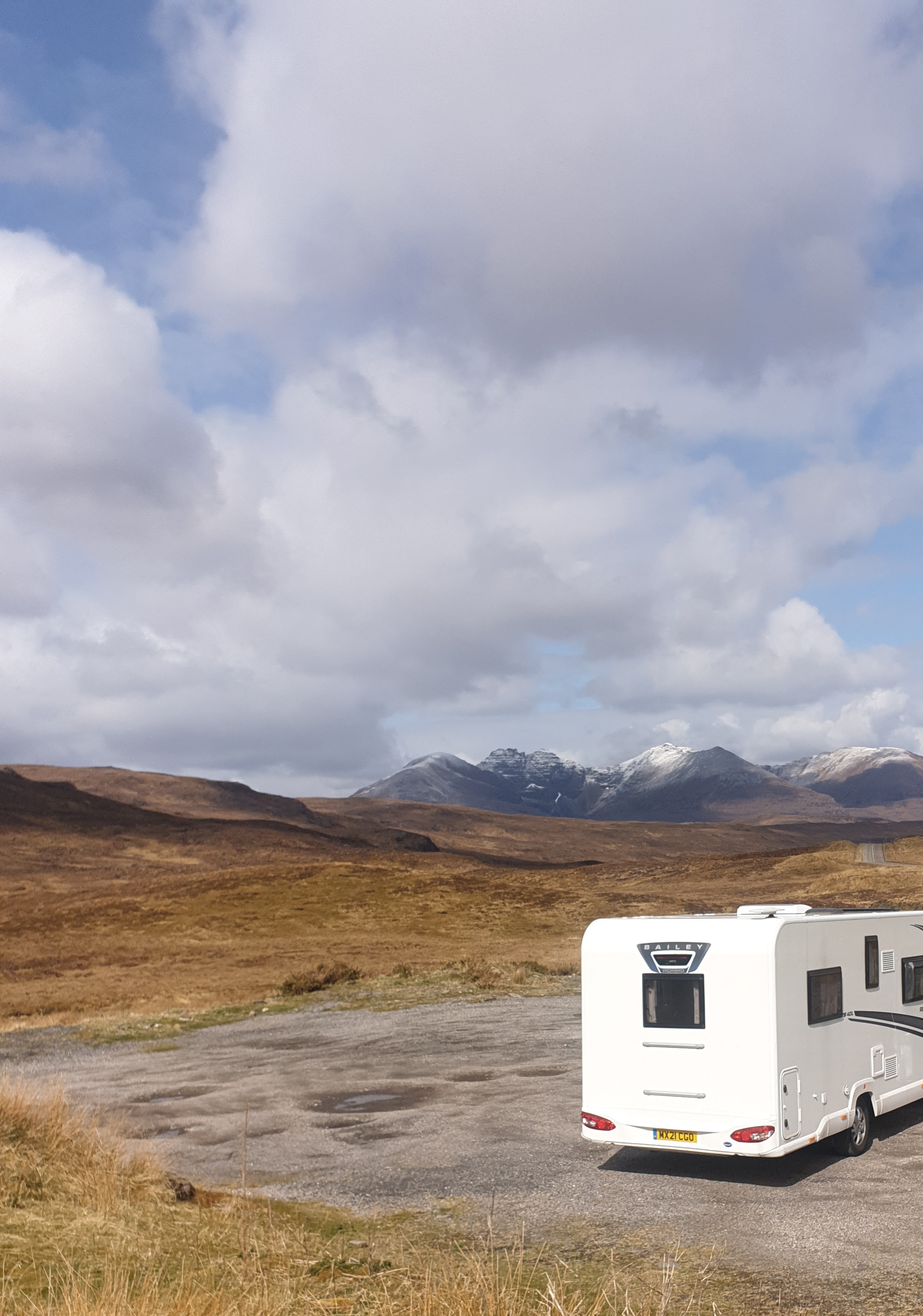 Our motorhome parked beside open moorland with snow-dusted mountains beneath a cloudy sky.